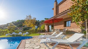 A poolside area with lounge chairs, a red umbrella, and a stone-tiled patio. - Llevant 2 in Lloret de Mar (Lloret de Mar)