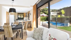 A modern living room with a large window, a dining area, and a view of a swimming pool. - Llevant 2 in Lloret de Mar (Lloret de Mar)