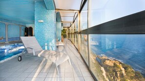 An indoor swimming pool with clear glass walls, a tiled floor, and a view of the sea. - Canyelles in Lloret de Mar (Lloret de Mar)
