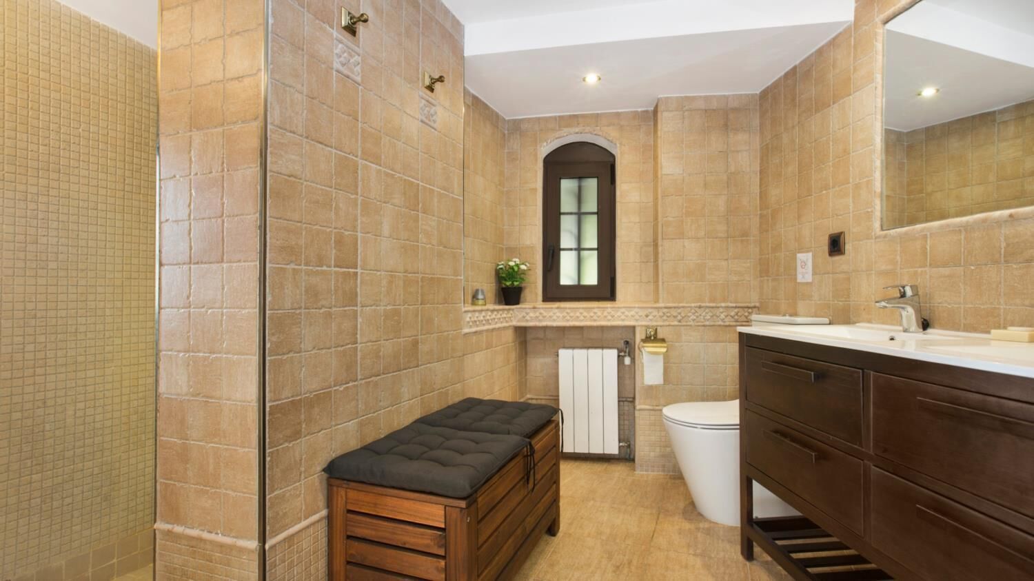 Een badkamer met een houten bankje, toilet, wastafel en spiegel.