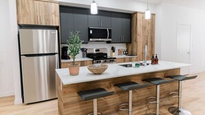 Una cocina moderna con un refrigerador de acero inoxidable, un microondas y una estufa. Hay armarios de madera y una encimera blanca.