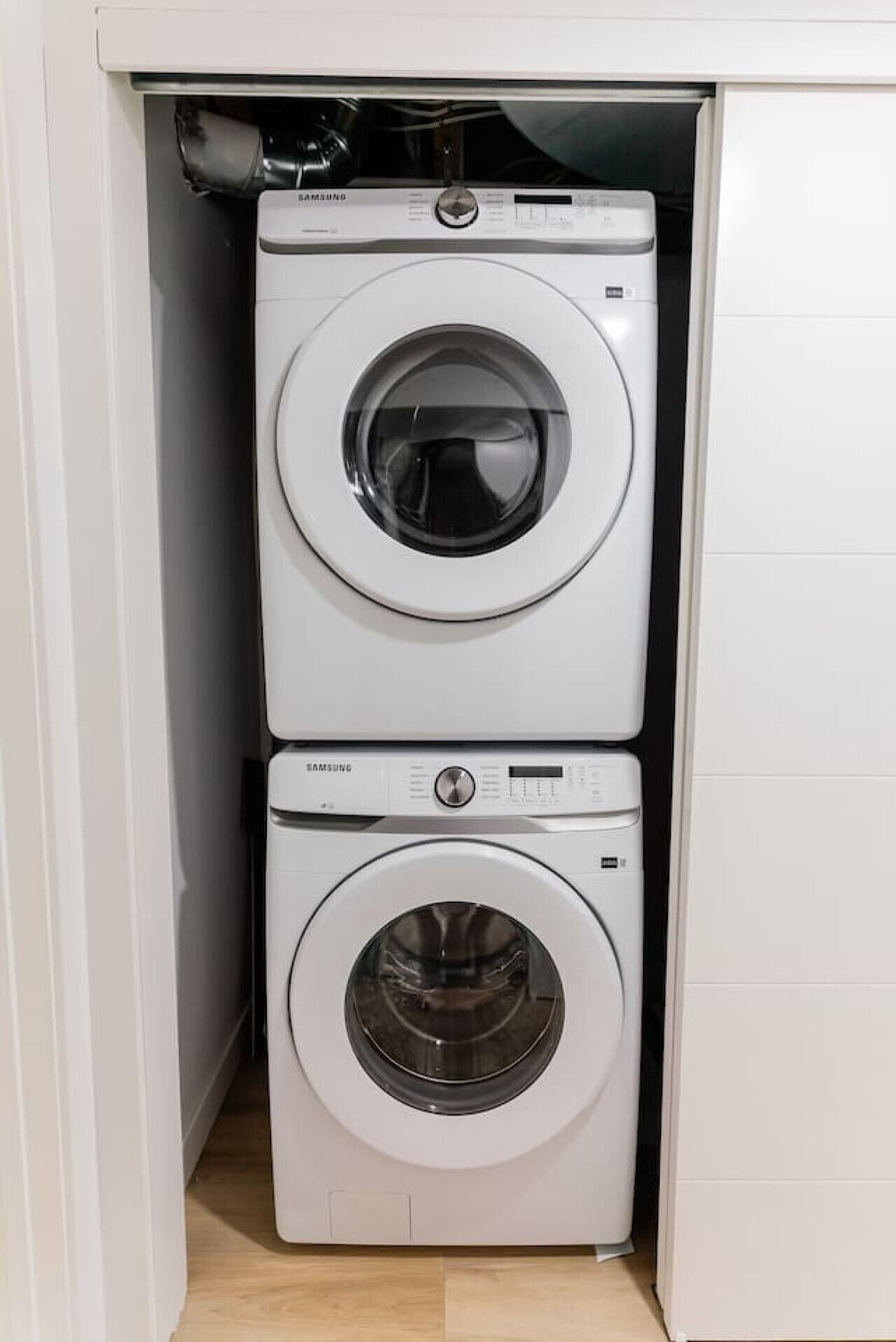 A compact laundry room with two Samsung washing machines, one above the other, in a white tiled space.