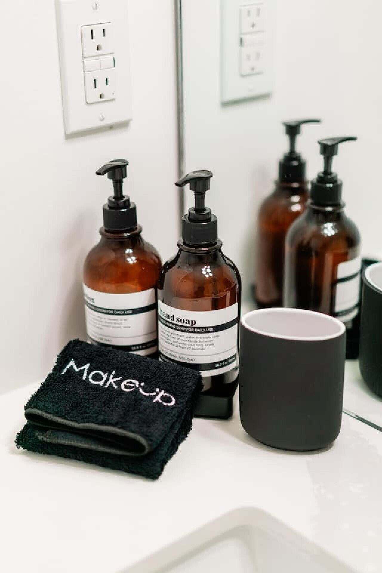 A bathroom vanity with a black towel labeled "Makeup," two bottles of hand soap, and a black mug.