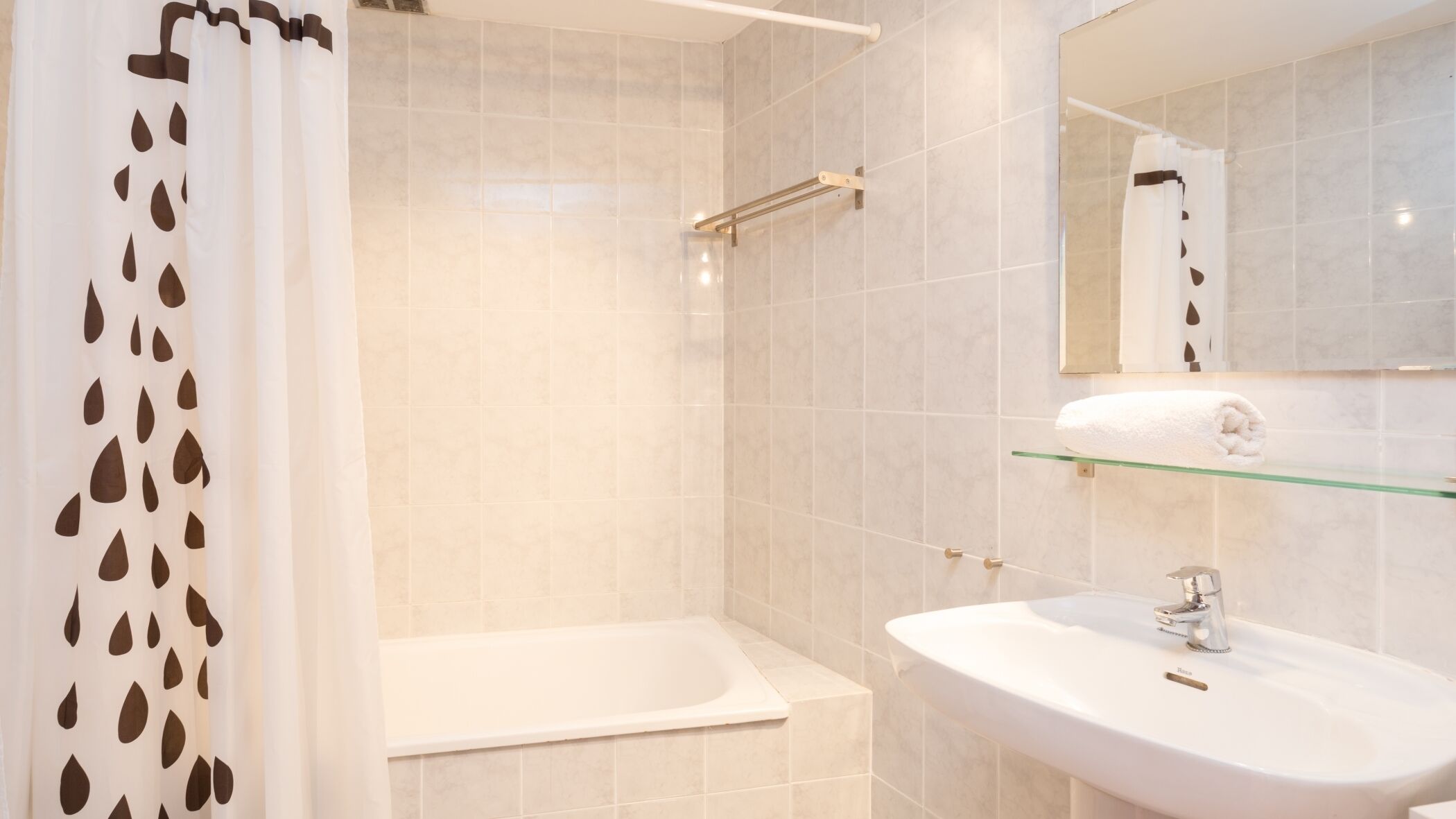 Un baño moderno con bañera, lavamanos y estante de vidrio.