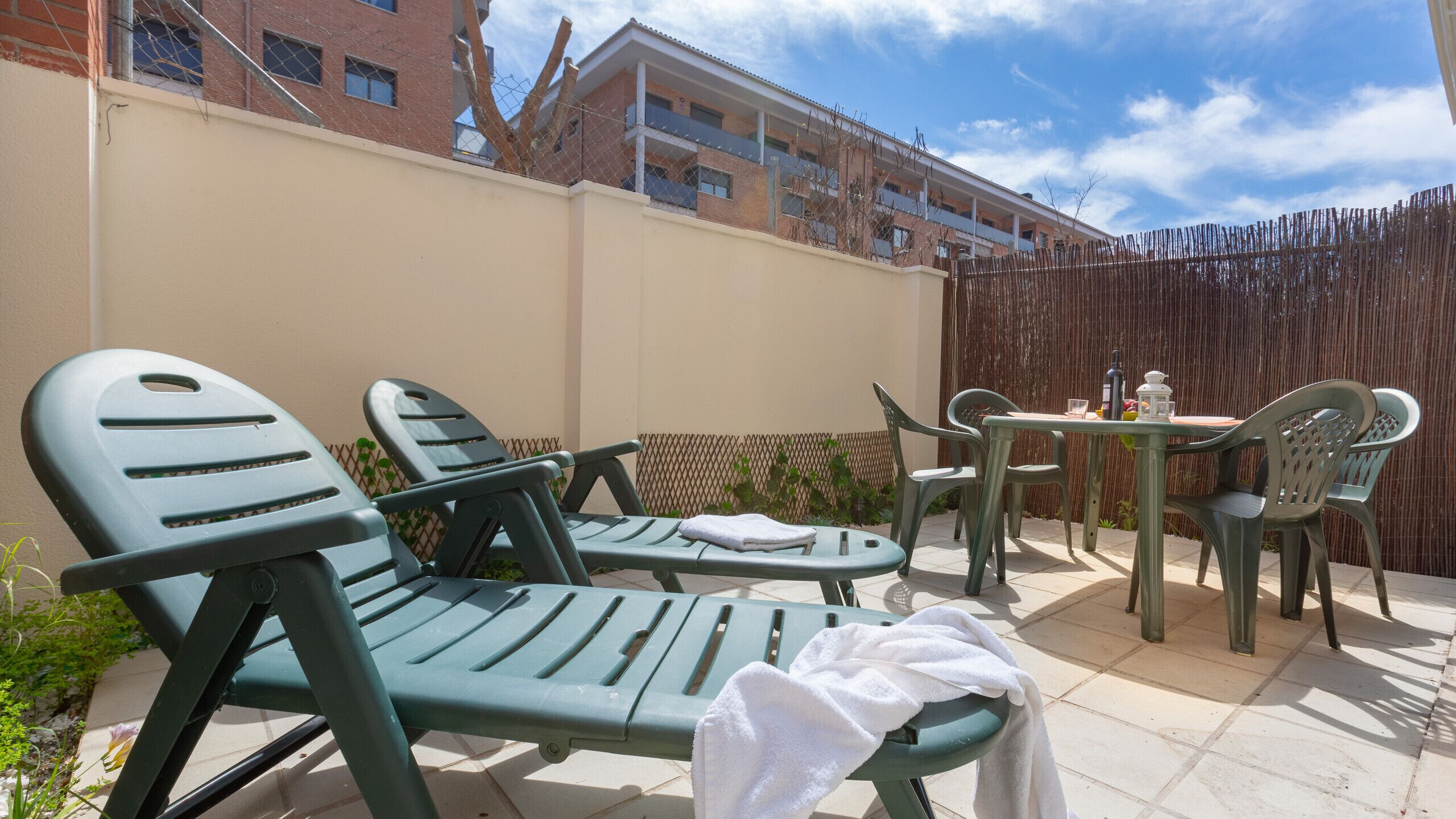 En terrasse med to grønne liggestole, et lille bord og en stol.