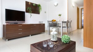 Una sala de estar moderna con televisor de pantalla plana, mueble de madera, mesa de comedor con sillas y plantas decorativas.