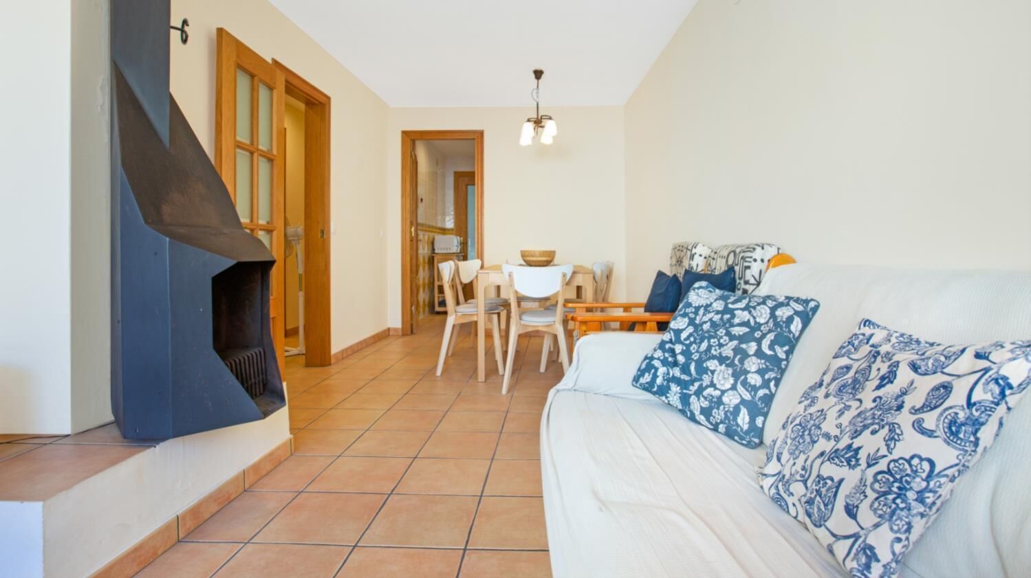 Un salon comprenant un canapé, des coussins à motifs, une cheminée, un coin repas avec des chaises et une table, ainsi qu’un luminaire au plafond.