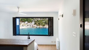 A room with a large window offering a view of a coastal town, a ceiling fan, and a radiator. - Mirador in Llafranc With 4 Bedrooms and 4 Bathrooms (Palafrugell)