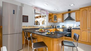 Une cuisine moderne dotée d’un îlot central, d’appareils électroménagers en acier inoxydable, de meubles en bois et de tabourets de bar.