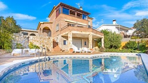 Une maison à deux étages dotée d’une piscine, de murs en pierre et d’un patio couvert avec des chaises longues.