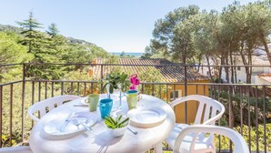 A balcony with a table set for two, overlooking a coastal area with trees and buildings. - Carena 1 in Llafranc (Palafrugell)