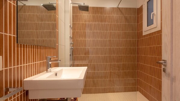 Un baño con lavamanos blanco, ducha con cabezal de ducha de mano y espejo.
