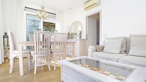 Egy nappali, melyben egy üveg asztallapú dohányzóasztal, egy fehér kanapé és egy étkező található, fából készült asztallal és székekkel.