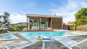 Un área moderna junto a la piscina con sillones de descanso, piscina y un edificio con grandes ventanales.