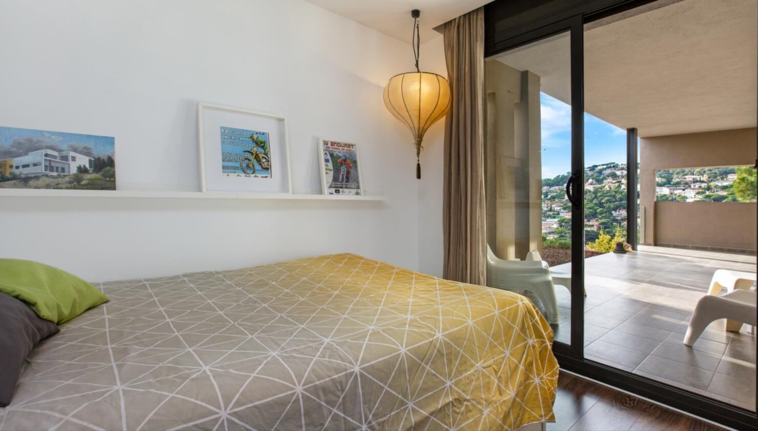 A bedroom with a bed, a balcony with a view, and wall art.