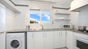 A kitchen with white cabinets, a washing machine, a microwave, and a stove. - Pandora 2 in Llafranc (Palafrugell)