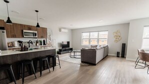 A modern kitchen with a central island, bar stools, and a dining area with a sofa and coffee table. - Cozy Winnipeg Getaway - Near The Forks & Hospital (Winnipeg)