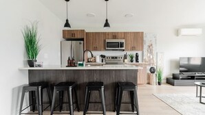 A modern kitchen with a central island, bar stools, a microwave, and a large flat-screen TV. - Cozy Winnipeg Getaway - Near The Forks & Hospital (Winnipeg)