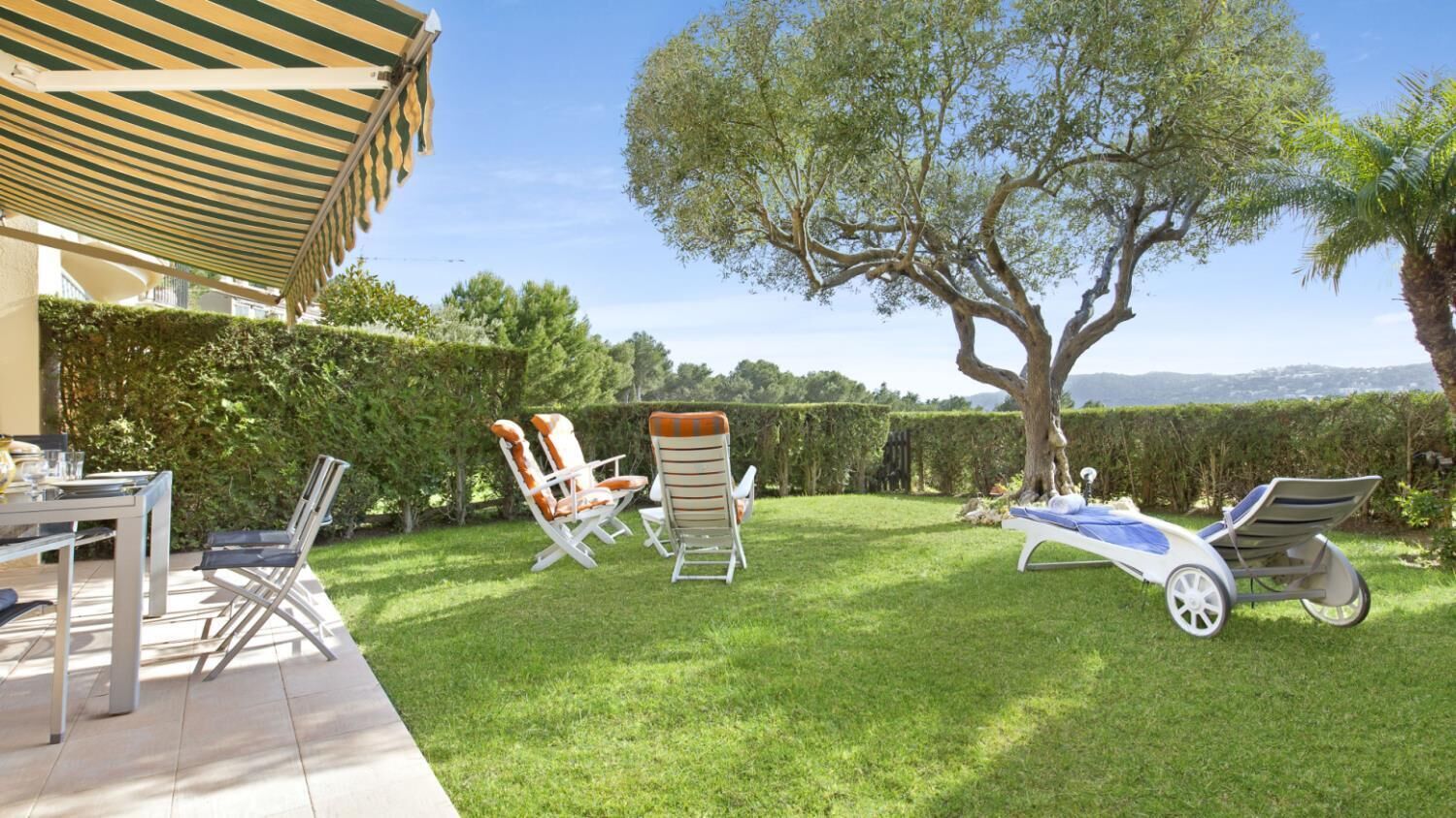 Eine Terrasse mit Tisch und Stühlen, ein großer Baum und freier Blick auf die Landschaft.