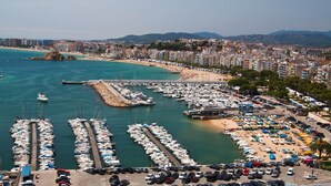 A marina with numerous boats docked, a beach with umbrellas, and a cityscape in the background. - Sa Palomera in Blanes (Blanes)