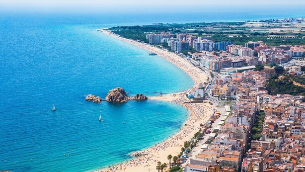 Un paisaje urbano costero con playa, edificios y un promontorio rocoso.