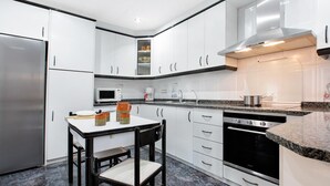 Una cocina moderna con armarios blancos, un refrigerador de acero inoxidable, un microondas, una cafetera y una estufa.
