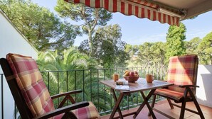 A balcony with two plaid chairs, a table with a bowl of fruit and two mugs, and a striped awning. - Cliper C 3 in Llafranc (Palafrugell)