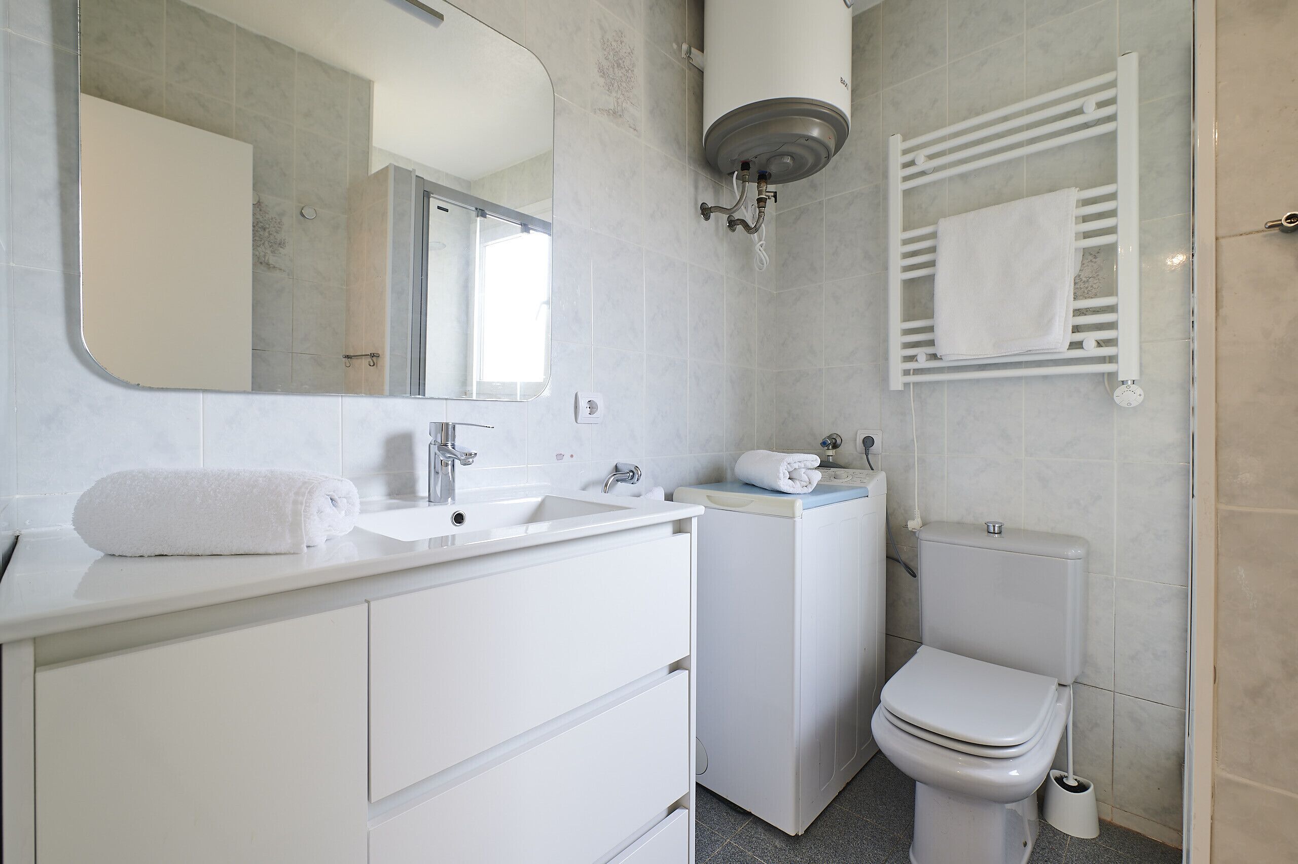 A modern bathroom with a sink, mirror, toilet, and towel rack.