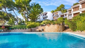 A swimming pool surrounded by stone walls and lush greenery, with multi-story buildings in the background. - Cliper C 3 in Llafranc (Palafrugell)