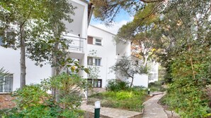 Ein weißes Gebäude mit mehreren Balkonen, umgeben von viel Grün und einem Steinweg.
