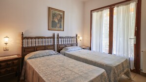 A bedroom with two beds, a wooden headboard, a nightstand, a wall-mounted light, and a window with curtains. - Masso in Llafranc With 3 Bedrooms and 1 Bathrooms (Palafrugell)