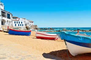 A beach with several boats tied to the shore, a building with arches, and the sea in the background. - Masso in Llafranc With 3 Bedrooms and 1 Bathrooms (Palafrugell)