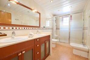 Un baño moderno con dos lavamanos, un espejo grande, cabina de ducha e inodoro.