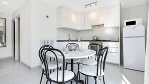 Una cocina moderna con armarios blancos, una mesa redonda de comedor con cuatro sillas y un refrigerador.