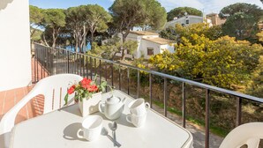 Un balcón con una mesa dispuesta para dos personas, con un jarrón de flores rojas, una tetera y dos tazas.