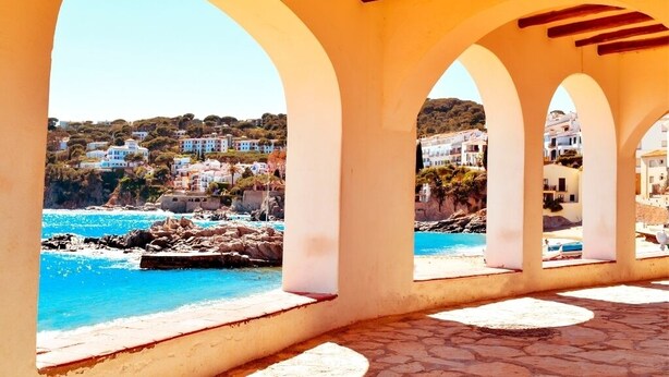 A coastal view through a series of arches overlooking a beach and a hillside settlement. - Llado 2 in Calella de Palafrugell (Palafrugell)