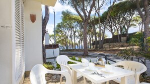 Eine Terrasse mit weißen Plastikstühlen und einem Esstisch, mit Blick auf eine natürliche Landschaft mit Bäumen und Meer.