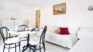 A white room with a round dining table, two black chairs, a white sofa with red and striped pillows, and a painting on the wall. - Ancora 08 in Llafranc (Palafrugell)
