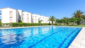 Una piscina con acqua cristallina, circondata da un edificio con numerosi balconi e palme.