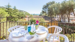 A balcony with a table set for two, overlooking a scenic view of trees and a distant coastline. - Carena 2 in Llafranc (Palafrugell)