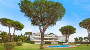 Un immeuble moderne à plusieurs étages, doté d’une piscine, entouré de pelouses et d’arbres bien entretenus.