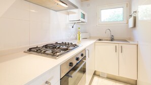 Moderni keittiö, jossa on valkoiset kaapit, kaasuliesi, uuni, mikroaaltouuni ja ikkuna tiskialtaan yläpuolella.