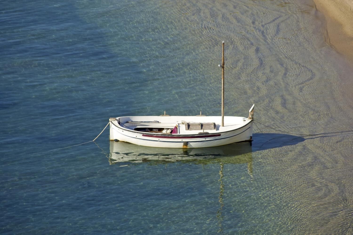 Ein kleines Boot liegt vor einer Sandküste in klarem Wasser vor Anker.