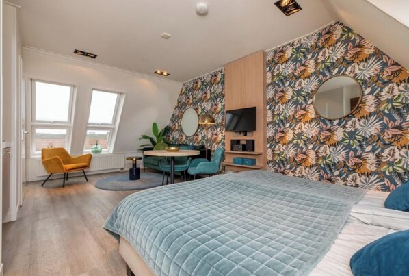 Un dormitorio moderno con una cama grande, un escritorio y una silla. Hay dos ventanas y un espejo en la pared.