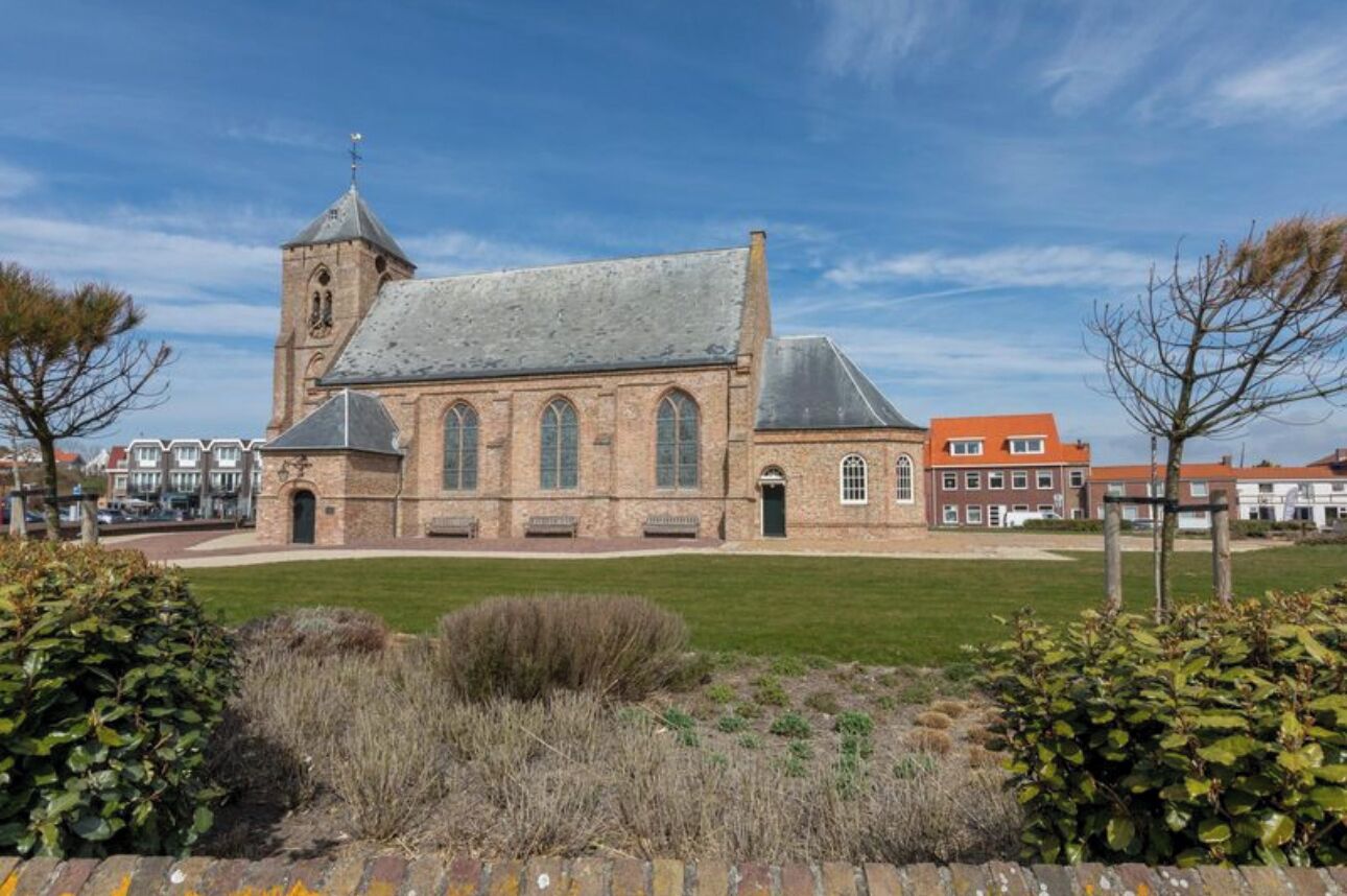 A historic church with a prominent tower and arched windows, surrounded by a well-maintained lawn and mature trees.