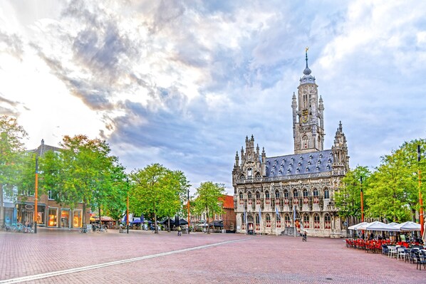 A historic building with intricate architecture, a prominent tower, and a paved square with outdoor seating. - Appartement - Langstraat 5B Zoutelande (Zoutelande)
