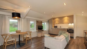 Una sala de estar moderna con sofá, mesa de comedor y sillas. Cuenta con una zona de cocina con armarios y un televisor.