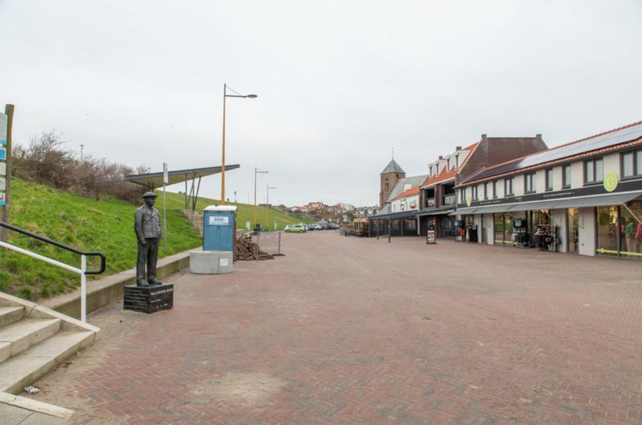 A paved street with a statue, a building with a red roof, and a signboard.