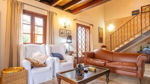 A living room with a white armchair, a brown leather sofa, a wooden coffee table, and a staircase in the background. - Sa Xigala in Algaida (Algaida)