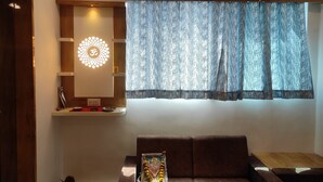 A living room with a sofa, a decorative wall piece, and a window with patterned curtains. - HOTEL SAVERA (Ahmedabad)